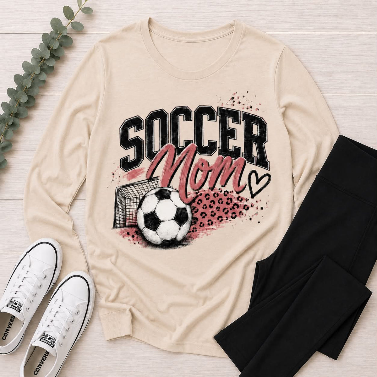Cream crewneck long sleeve Soccer Mom graphic tee featuring pink lettering, soccer ball, goal and leopard print accents.