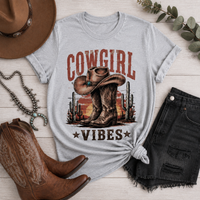 Cowgirl Vibes western graphic apparel featuring cowboy boots, cowgirl hat, cacti and desert sunset design