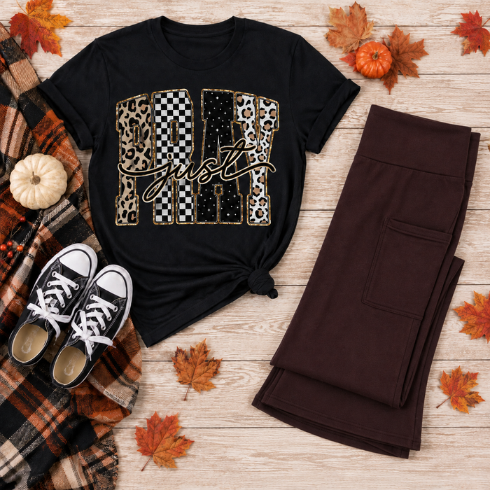 Black Pray Just Pray graphic T-shirt with leopard, cow print, checkerboard, and star lettering styled with brown leggings and fall accessories.
