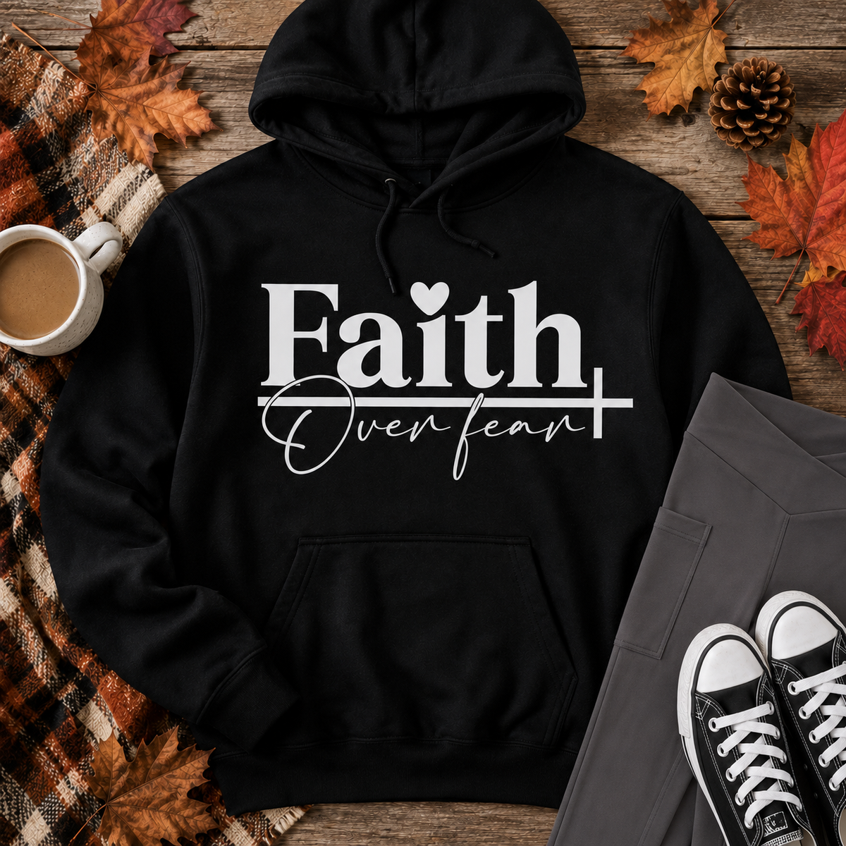 Black Faith Over Fear graphic hoodie styled in a fall flat lay with charcoal crossover pocket leggings, black sneakers, a plaid blanket, coffee, and autumn leaves.