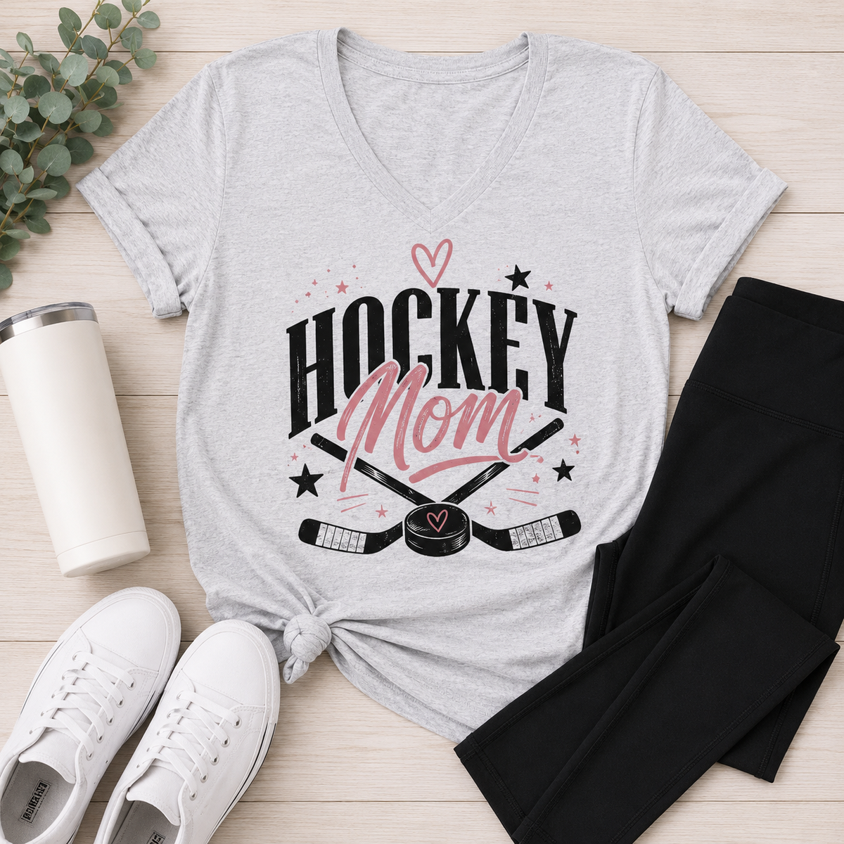 Heather gray v-neck Hockey Mom graphic tee featuring a black and pink hockey design styled with black leggings and white sneakers.