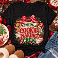 A black V-neck t-shirt with a festive 'Christmas Cookie Baking Crew' graphic, styled in a holiday flat-lay with jeans, slippers, cookies, and red plaid fabric.