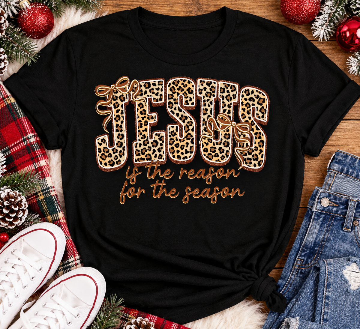 Jesus Is the Reason for the Season Christmas graphic shirt featuring bold leopard print JESUS lettering, decorative gold bows, and gold script. Faith-inspired holiday apparel available in red and black with four style options.