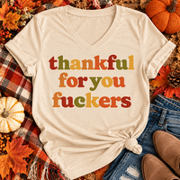 Funny Thankful for You Fuckers Thanksgiving graphic tee featuring bold retro lettering in burnt orange, mustard yellow, olive green, and rust red. Women's fall-inspired short sleeve crewneck shirt available in beige and brown, perfect for Thanksgiving and Friendsgiving.
