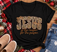 Jesus Is the Reason for the Season Christmas graphic shirt featuring bold leopard print JESUS lettering, decorative gold bows, and gold script. Faith-inspired holiday apparel available in red and black with four style options.