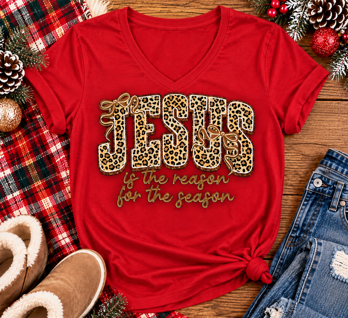 Jesus Is the Reason for the Season Christmas graphic shirt featuring bold leopard print JESUS lettering, decorative gold bows, and gold script. Faith-inspired holiday apparel available in red and black with four style options.
