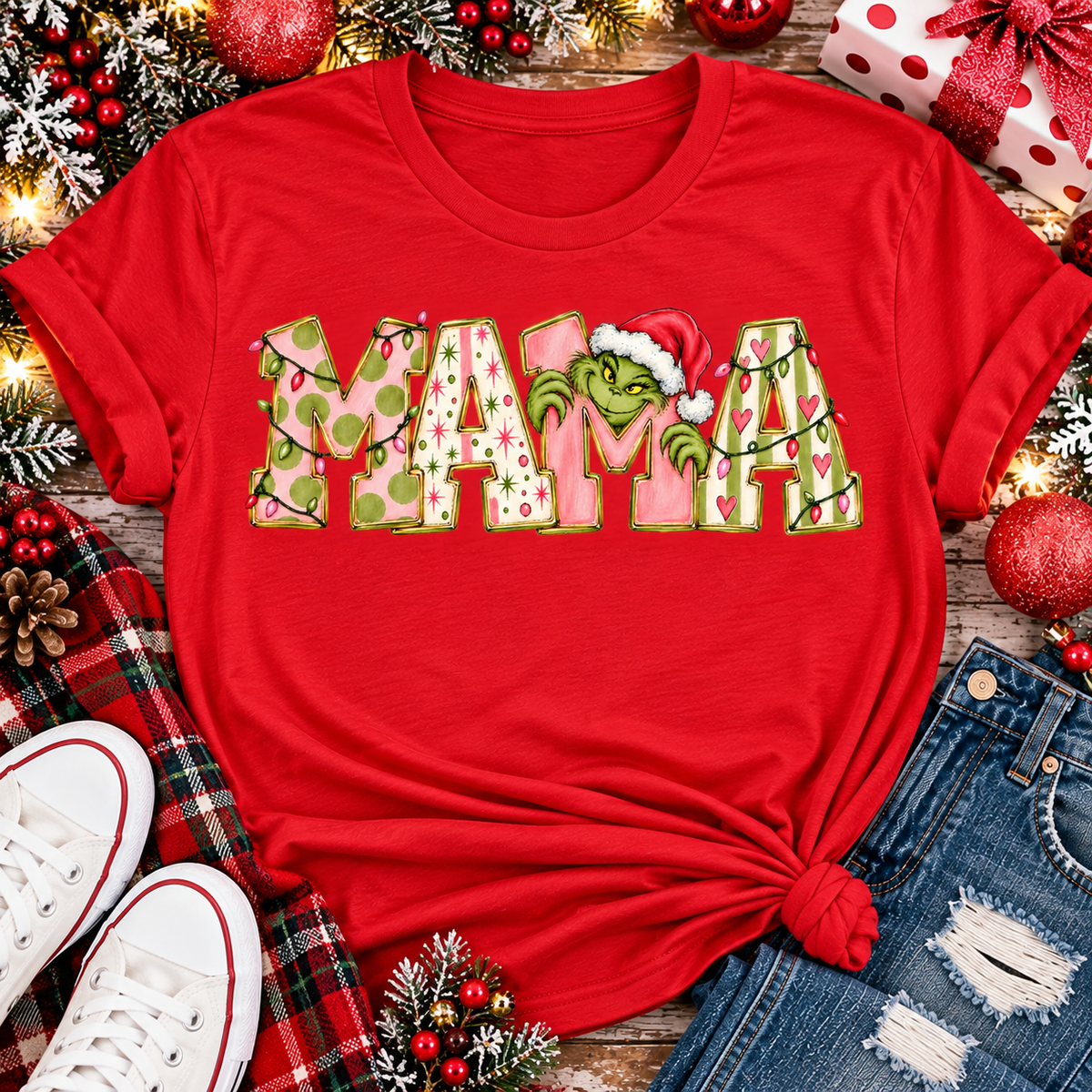 Christmas MAMA graphic shirt featuring pink and green patterned lettering, colorful holiday lights, and a Grinch-inspired character wearing a Santa hat.