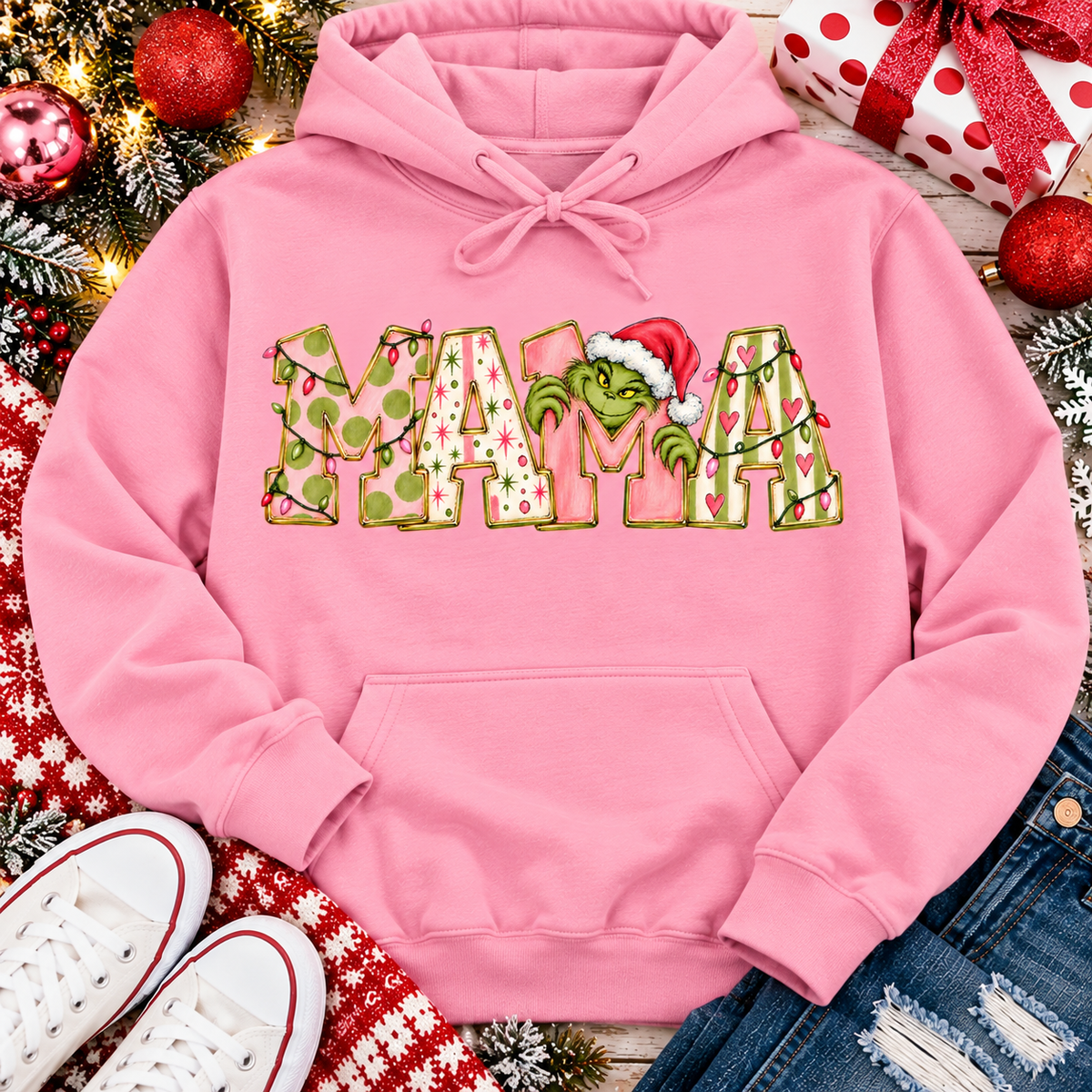 Christmas MAMA graphic shirt featuring pink and green patterned lettering, colorful holiday lights, and a Grinch-inspired character wearing a Santa hat.