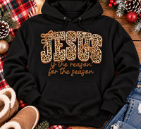 Jesus Is the Reason for the Season Christmas graphic shirt featuring bold leopard print JESUS lettering, decorative gold bows, and gold script. Faith-inspired holiday apparel available in red and black with four style options.
