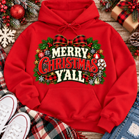 Merry Christmas Y'all graphic apparel featuring vintage red, green, and cream lettering with a festive buffalo plaid bow, Christmas ornaments, pine greenery, and rustic holiday decorations. Southern Christmas graphic available in two colors and four styles, including short sleeve crewneck, V-neck, long sleeve, and hoodie.