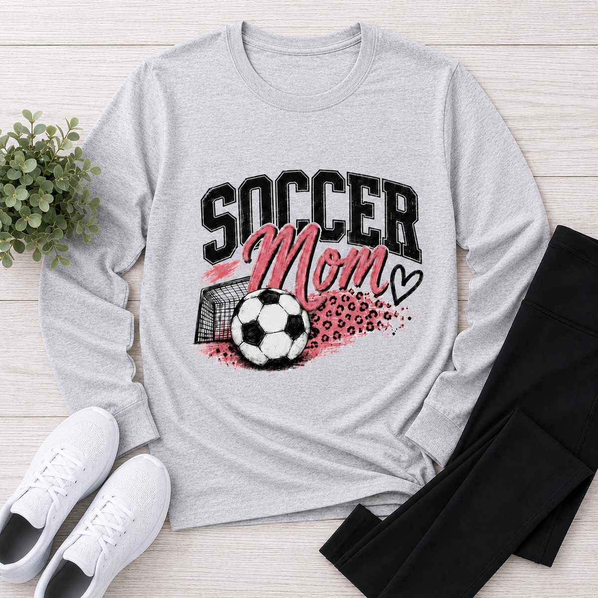 Gray crewneck long sleeve Soccer Mom graphic shirt with pink and black soccer design, styled with black leggings and white sneakers.