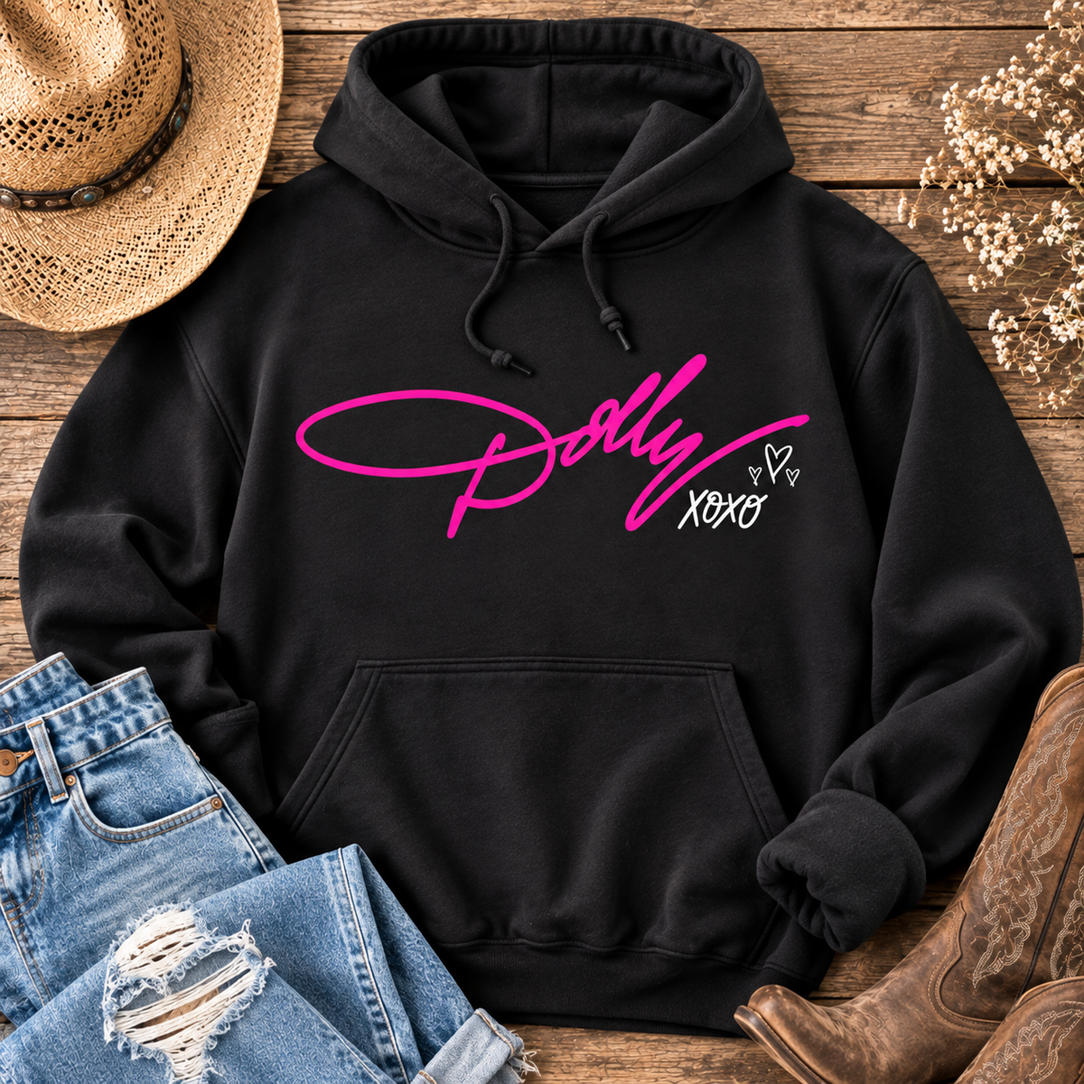 Black Dolly XOXO graphic hoodie featuring bright pink Dolly script with white XOXO and heart details, styled with distressed jeans and cowboy boots.